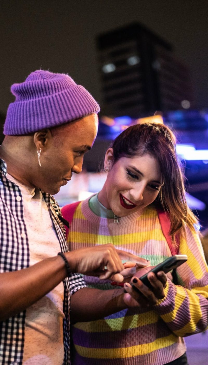 Young couple (or friends) using mobile phone at festival by the night - including a transgender person